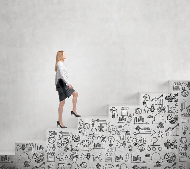 Young businesswoman going steadily up a a concrete stairs with drawn business icons on it along a concrete wall. Concept of career growth. career change