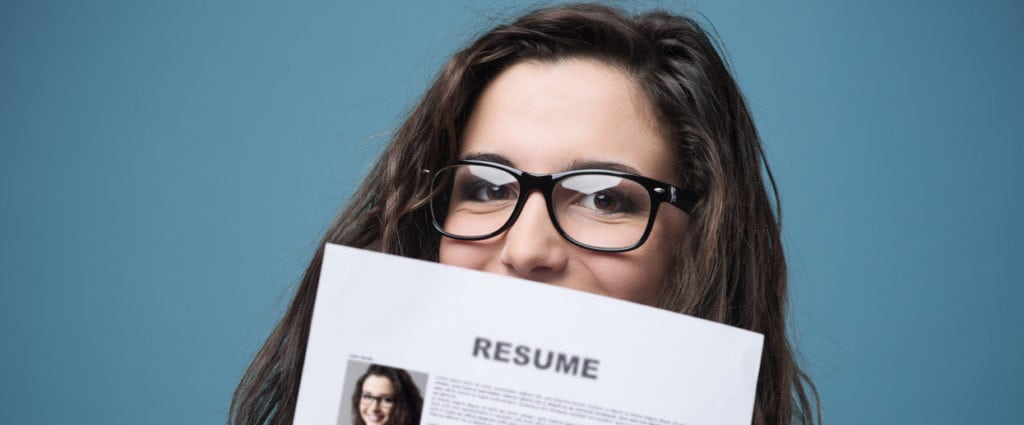 Young woman with glasses holding resume in front of face