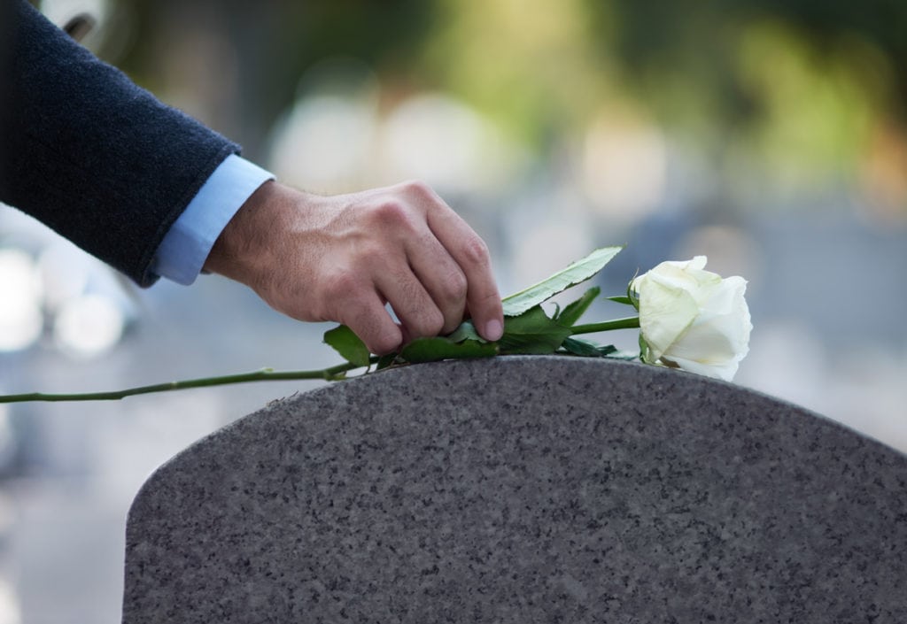 Cropped shot of a man placing a white rose on a grave of a spouse