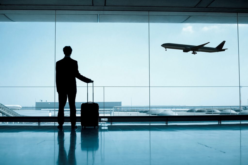 Businessman standing in airport watching airplane take off with travel hacks