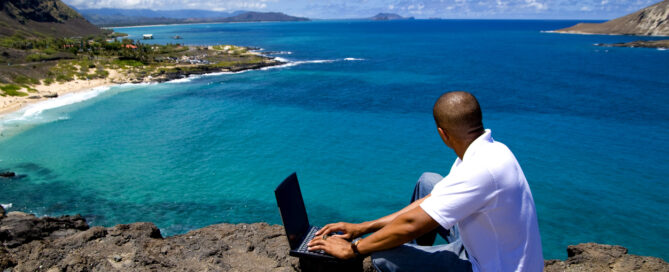 Job seeker looking out over Hawaiian coastline while searching for jobs on his laptop